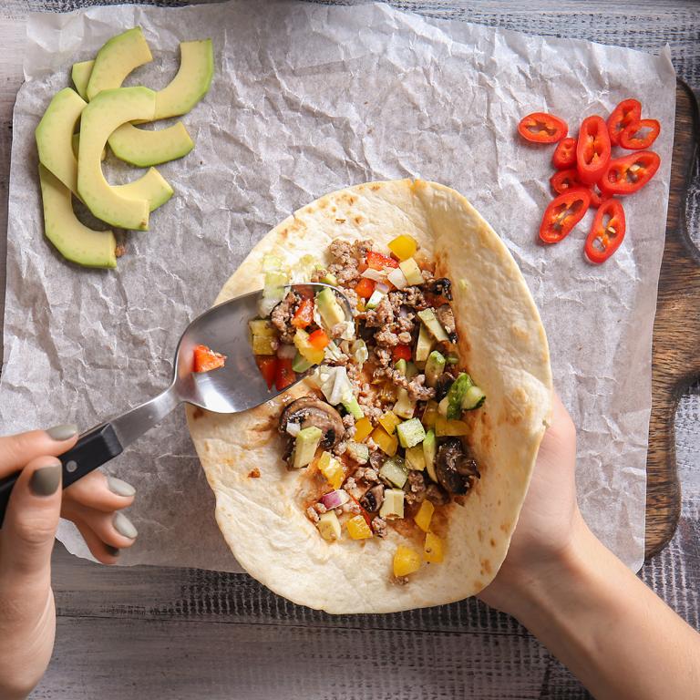 person's hands filling a tortilla to make a burrito at home